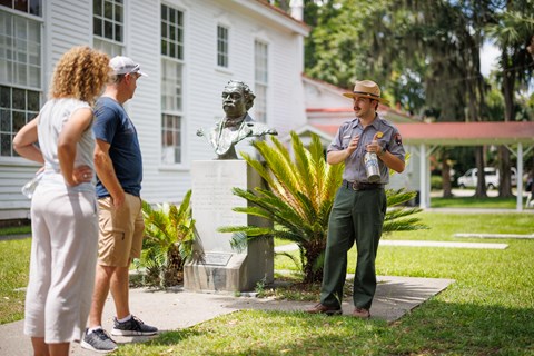 A ranger talks to two visitors in front of a bust of Robert Smalls.