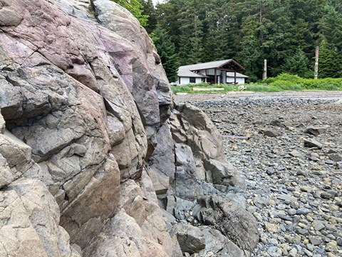 Bus-sized outcrop of almost uniformly gray rock with perceptible grains on a tidal flat