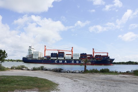 A large cargo ship on a river with a gravel driveway on land.