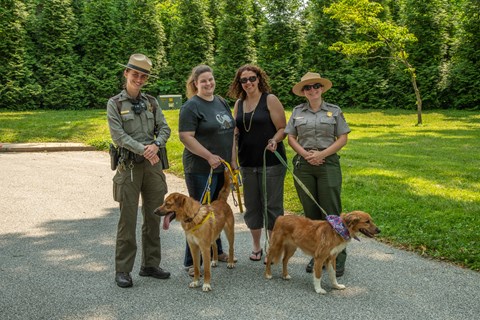 Two visitors with dogs on leashes pose with two park rangers.