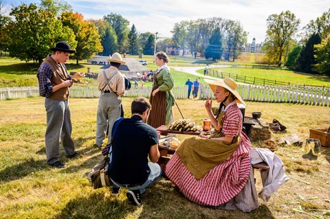 Living historians eating food at a wooden table on a sunny day.