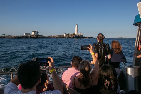 People on a boat taking pictures or looking at a white lighthouse on a rocky island.