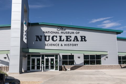 A light grey building, with a sign, with text that says National Museum of Nuclear Science & History