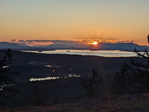 A view of a sunset from the top of a mountain, looking towards the ocean and islands.