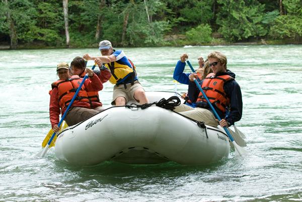 A group paddle a raft on a wide river.