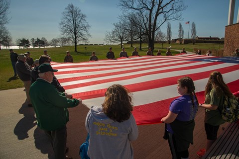 A group of visitors holding on to a large Star-Spangled Banner Flag.