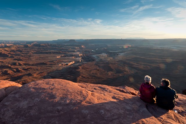 Two hikers sitting on the edge of Green River Overlook at sunset