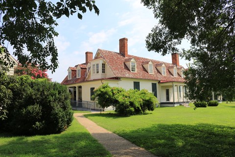 White two-story building with red roof and two red chimneys, tree in foreground of image.