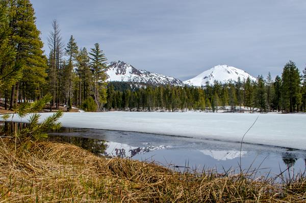 Two snow-covered volcanoes reflected in a small patch of unfrozen water backed by a frozen lake line