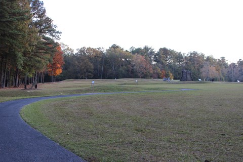 A paved trail winds through a field, past signs and toward a cannon and wooden tower.