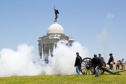 Living history volunteers fire a civil war cannon in front of a white, domed monument.
