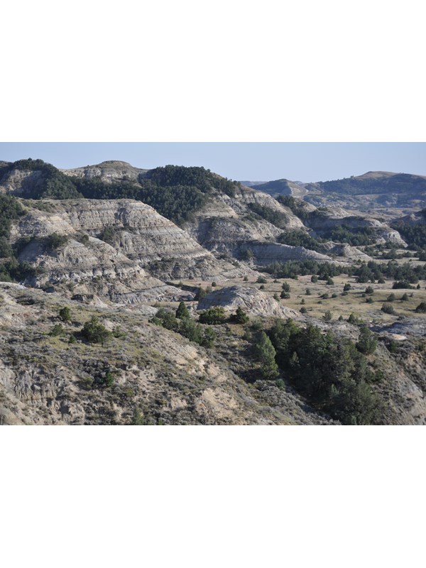 The badlands, including a view down into a sandy bottomed valley and large buttes under a cloudy sky