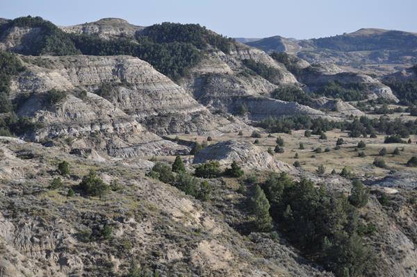 The badlands, including a view down into a sandy bottomed valley and large buttes under a cloudy sky