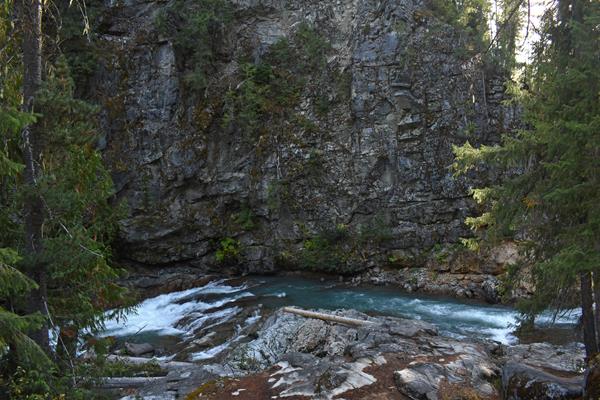 A rushing creek with clear green water under steep gray rocky cliffs