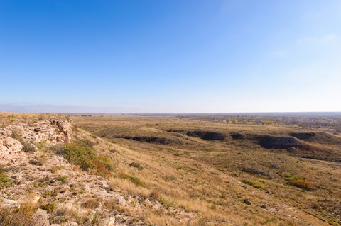 A rocky bluff looks out on a flat plain of sparse vegetation.