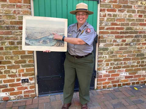 Ranger Karen in a flat hat holding a historic painting of new orleans
