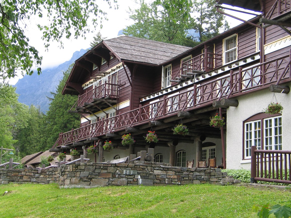 A rustic three-story lodge with dark brown wood and white stone decorated with hanging plants.