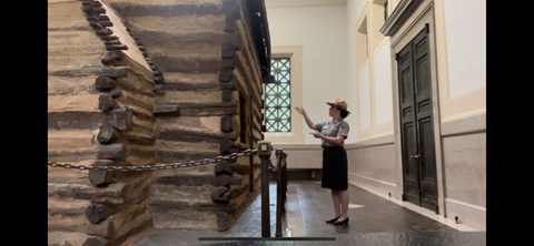 Ranger pointing at single room log cabin