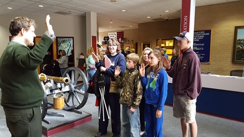 Park Ranger swears in a family of Junior Rangers next to cannon
