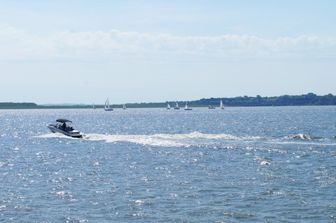 Motor boat on the Missouri making waves with various sail boats behind it.