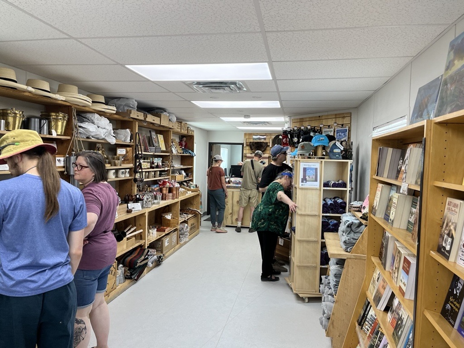 Visitors stand inside a narrow building and review items on wooden shelves.