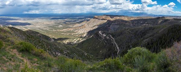 Wide landscape view of brush covered hills in foreground and mountain peaks in the distance.