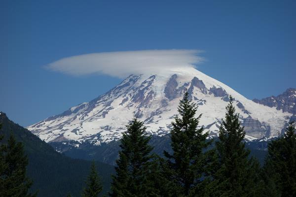 A glaciated mountain with lenticular clouds streaming from the peak.