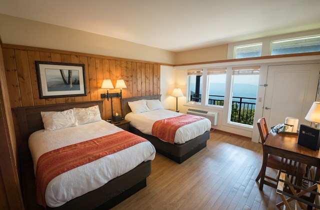 A hotel room with two beds and a view through the window of blue mountains.