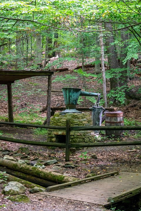 A stone oven with a metal caldron on top, draining into a wooden barrel.