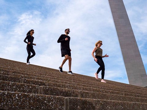 two women and a man jogging down the Grand Staircase in front of the Arch