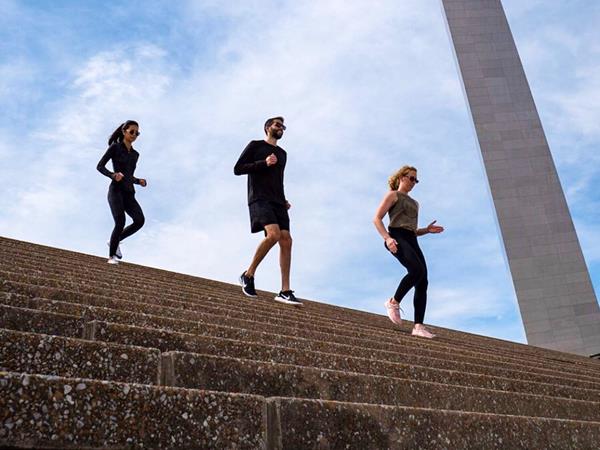 two women and a man jogging down the Grand Staircase in front of the Arch