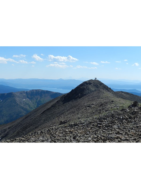 Two hikers enjoying the view of mountains in the distance from the summit of rocky mountain.