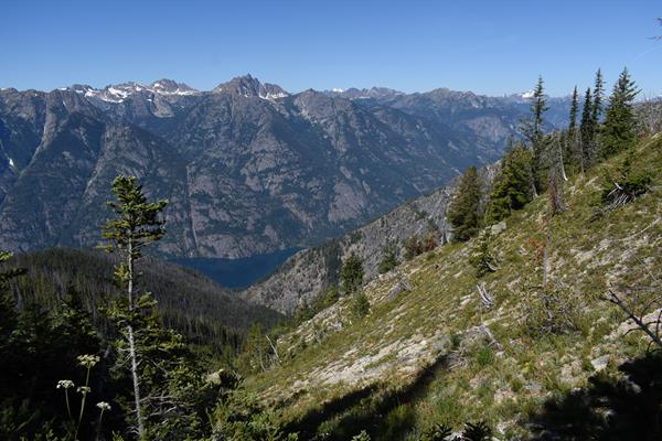 A view looking down past forested hills to steep mountains rising from a long, thin lake.