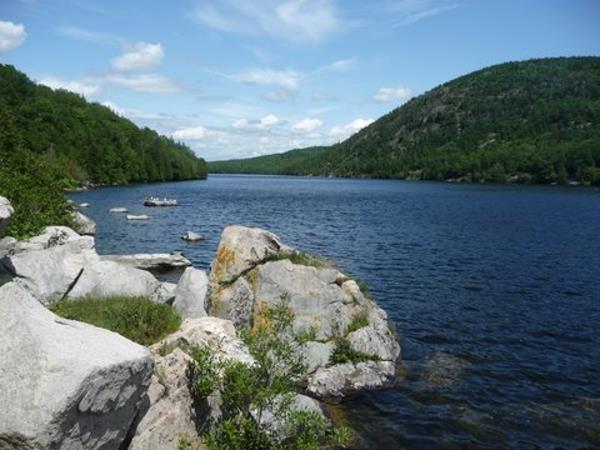 Large rocks in the foreground of a lake bordered by tree-covered hills
