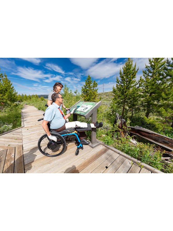 Visitors on a boardwalk view a low profile wayside exhibit