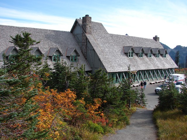 A rustic gray building with green trim sits surrounded by fall foliage.