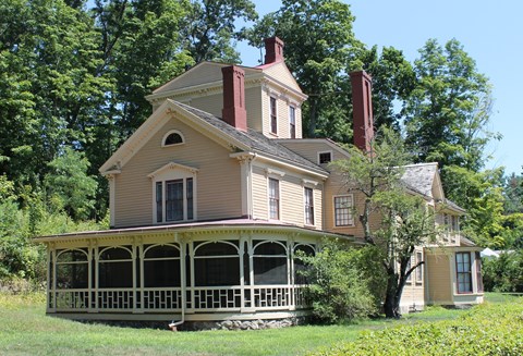 A four story house with tower sits on a hillside covered in trees