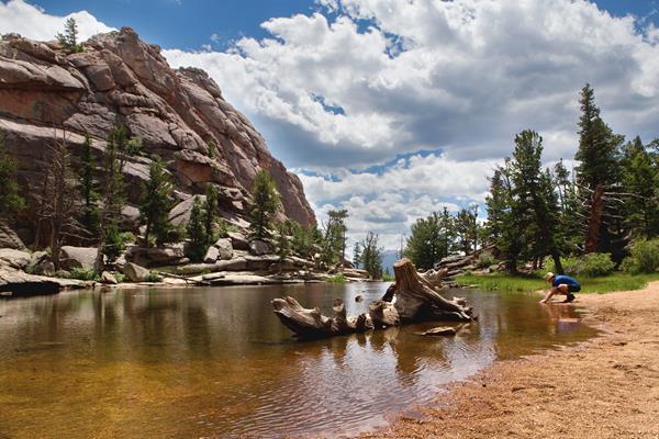 a person squats near the edge of a lake