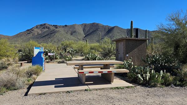 A single unshaded, wheelchair accessible, stone table sits on a slap of concrete.