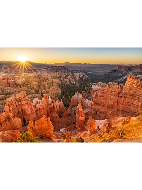 Looking down from above over a scenery of irregular red rocks with the sun rising behind them
