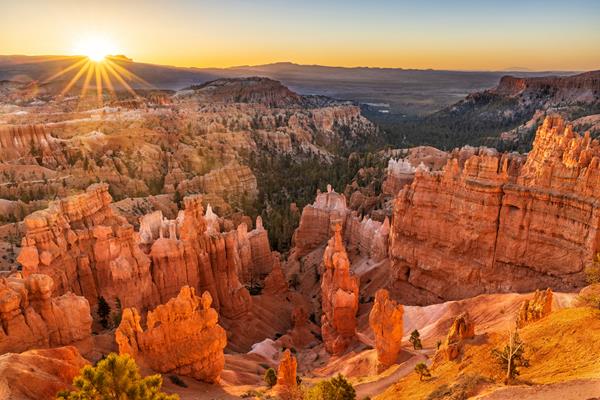 Looking down from above over a scenery of irregular red rocks with the sun rising behind them