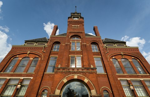 A red brick four story building with a clock tower stands tall against a partly cloudy sky.