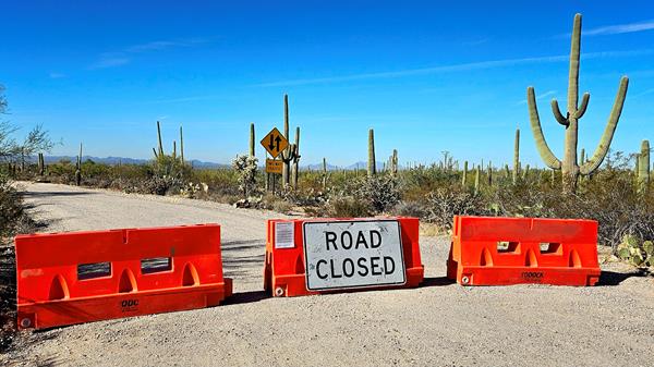 Three large orange barriers block the road. The center barrier has a sign reading "ROAD CLOSED"