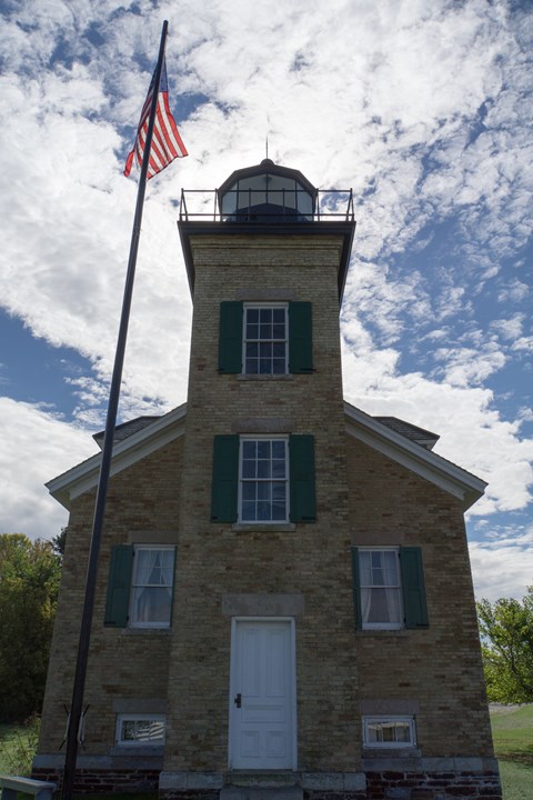 A lighthouse front is in shadows in front of a bright, cloudy sky