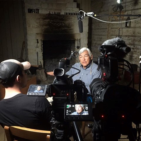 One man speaks facing a camera, second man watched playback on TV monitor
