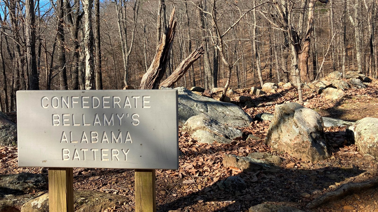 A gray sign in the foreground in front of boulders and a small mountain peak in the distance