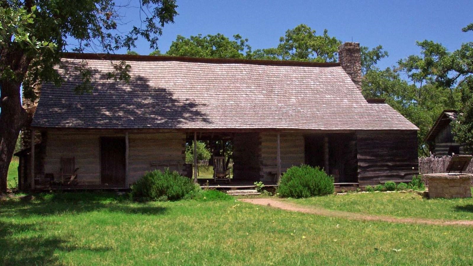 A log cabin with two rooms separated by a breezeway sits on green grass under a blue sky.
