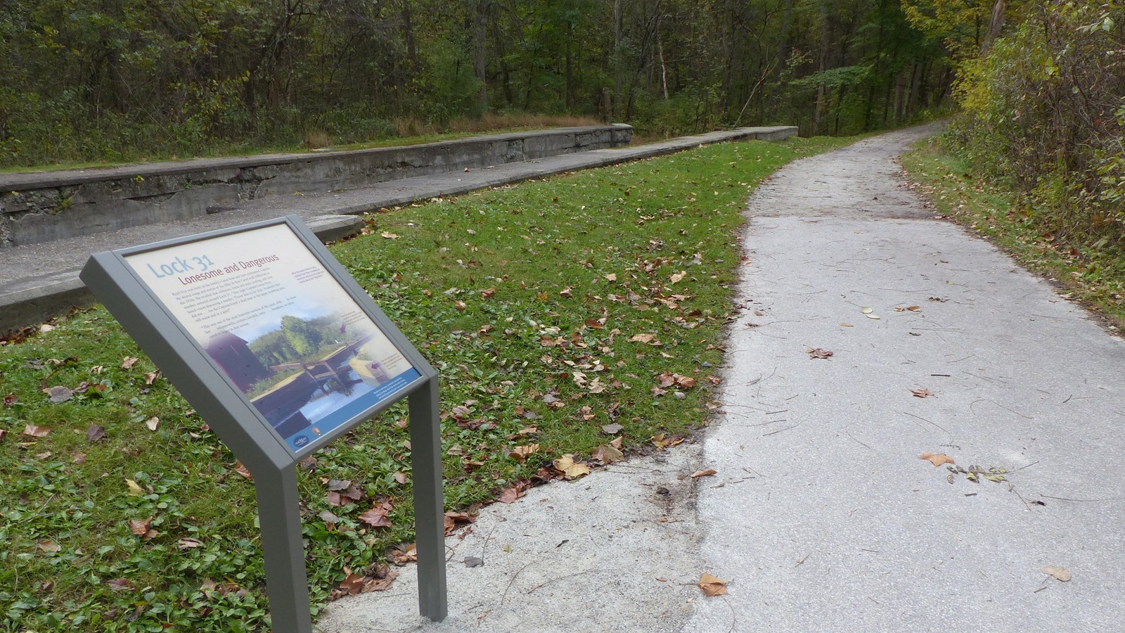 An exhibit overlooking a concrete canal lock next to an unpaved trail that bends out of view.