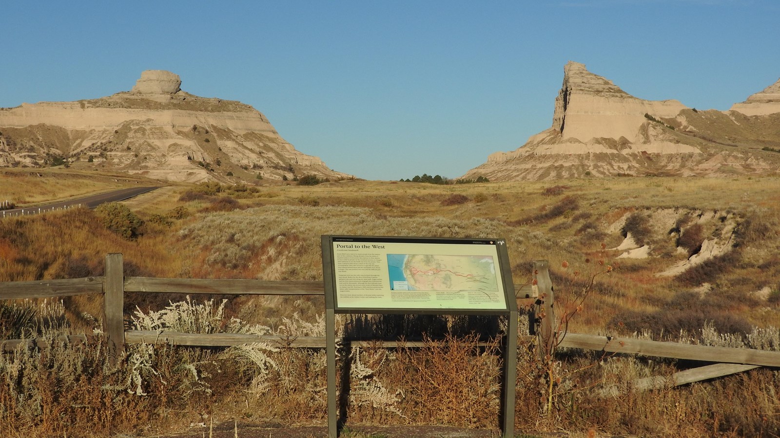 An interpretive wayside panel overlooks a gap between sandstone bluffs.