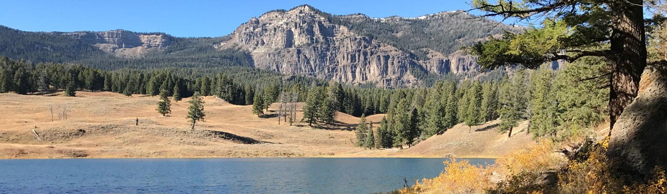 A lone hiker travels along the trail on the far side of the lake.